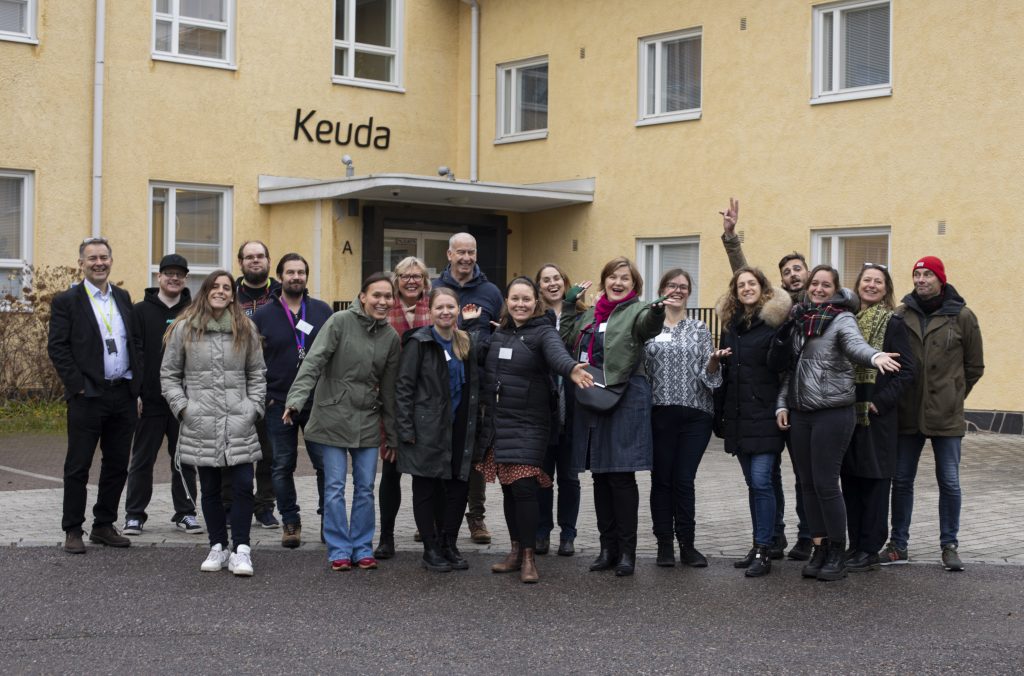 Ryhmä ihmisiä seisoo keltaisen rakennuksen edessä, jossa lukee oven päällä "Keuda".