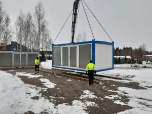 Suurta konttia lasketaan lumiselle maalle. Kaksi ihmistä on seuraamassa kontin asettamista maahan.