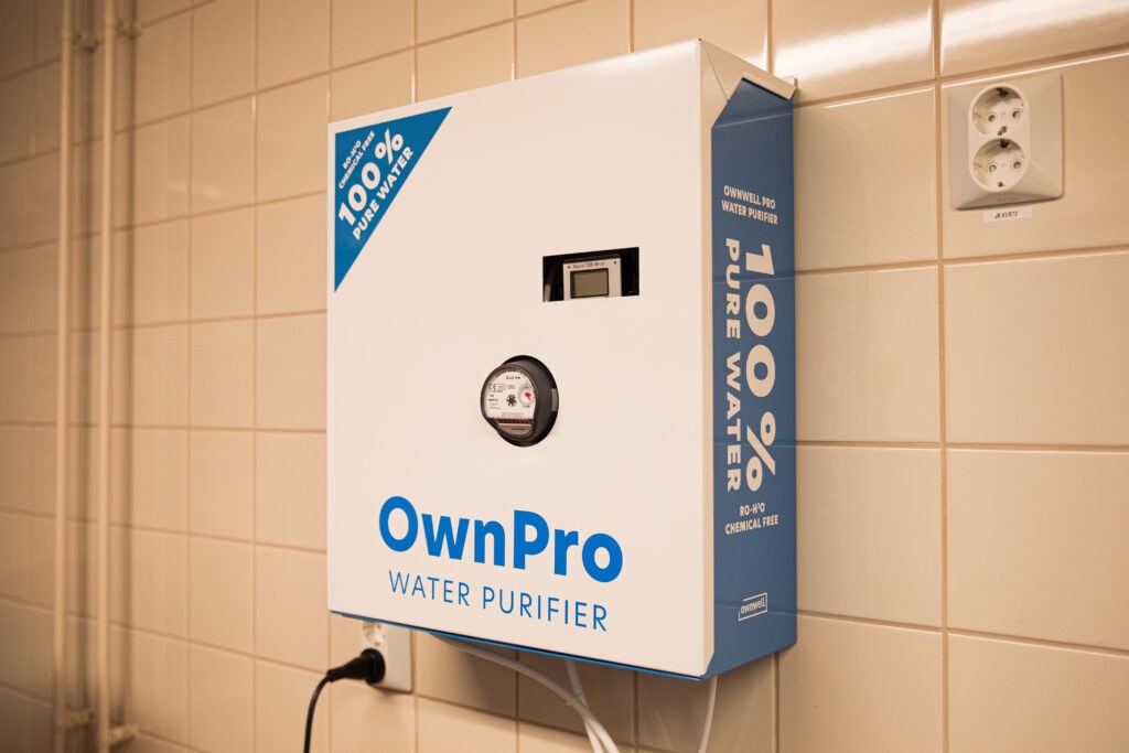 Valkoinen laatikko kiinnitetty laattaseinää vasten. Laatikossa lukee "OwnPro Water Purifier".